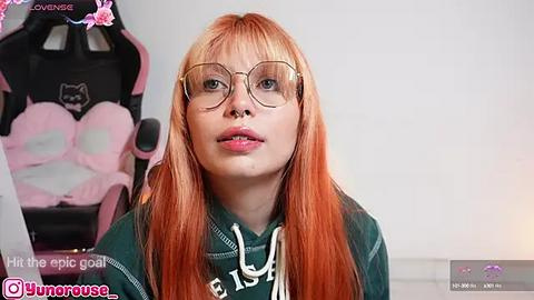 Media: Video of a young woman with long, orange hair and glasses, wearing a green hoodie, seated in a pink gaming chair, with text overlay \"Hit the epic goal!\