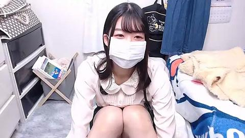 Media: Video of an Asian woman with long black hair, wearing a white mask, white blouse, and black skirt, sitting on a bed with a plush toy, in a tidy bedroom.