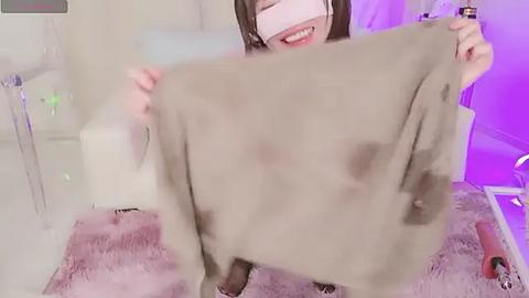 Media: A video of a smiling, fair-skinned woman with long brown hair, wearing VR goggles, holding a large, fluffy, brown and white cat on a pink shag rug in a softly lit, minimalist room.