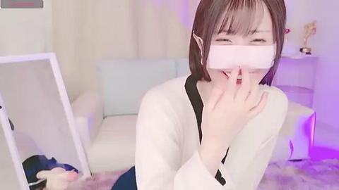 Media: Video of a young East Asian woman with straight brown hair, wearing a VR headset, smiling, in a light-filled room with a white couch and a mirror.