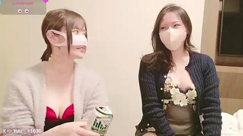 Media: Video of two East Asian women in a hotel room, both wearing surgical masks and light-colored cardigans. One holds a can of beer, the other a water bottle.