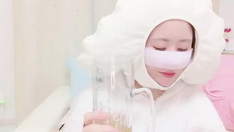 Media: Video of a young Asian woman wearing a white, fluffy cat mask with a clear plastic tube inserted into her nose, emitting a steady stream of air. She has light skin and is seated indoors, likely in a medical setting.