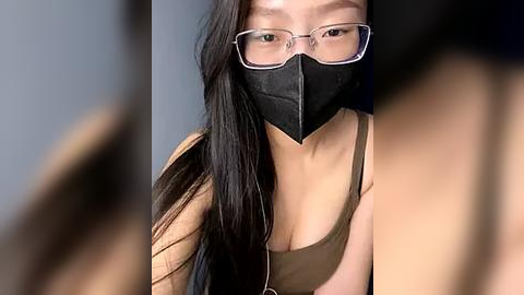 Media: Video of an East Asian woman with long black hair, wearing glasses, a black mask, and a tan tank top, blurred background, emphasizing her face.