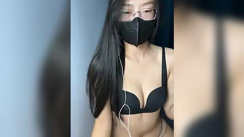 Media: Video of an Asian woman with long black hair, wearing a black bra and face mask, listening to white earphones, in a dimly lit room.