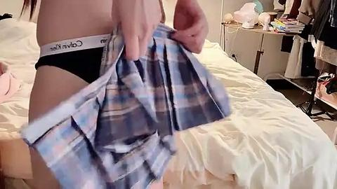 Media: A video of a person in a bedroom, pulling up a blue and white plaid shirt, revealing Calvin Klein black panties. Background shows a messy bed and scattered clothing.