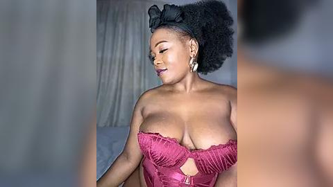 Media: Video of a voluptuous, dark-skinned woman with large breasts in a red lace bra, wearing a black headpiece and gold earrings, standing in a dimly lit bedroom with beige curtains.