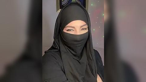 Media: Video of a woman with light skin, wearing a black niqab, green eyes, and a black headscarf, indoors, blurred background, soft lighting.