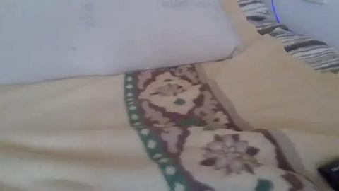 Media: A video of a bed with a beige sheet, green floral pillowcase, and a white pillow, with a blurred background.